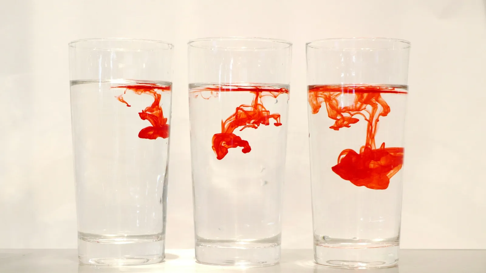 Red dye spreading in three glasses of water