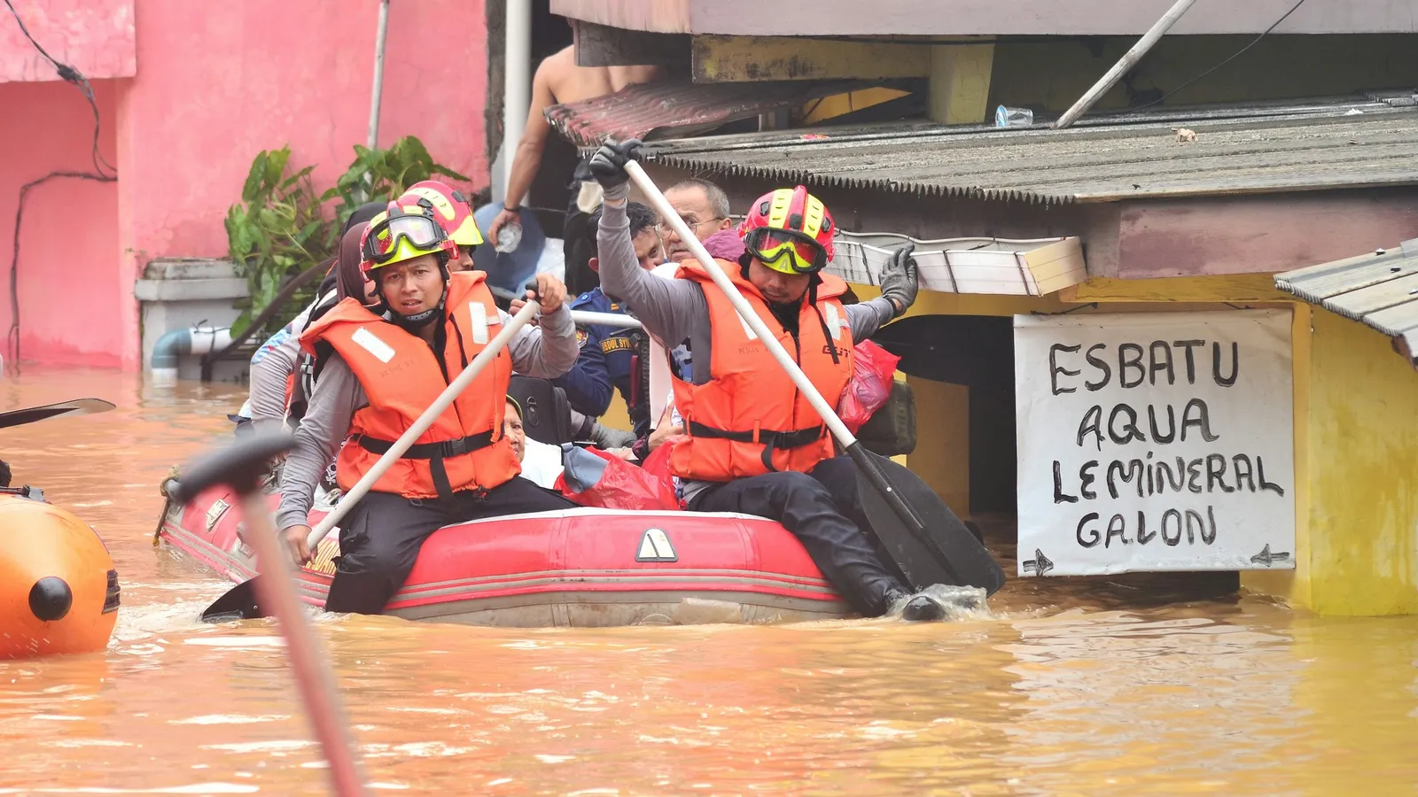 Rescue workers in life jackets steering a boat through floodwater