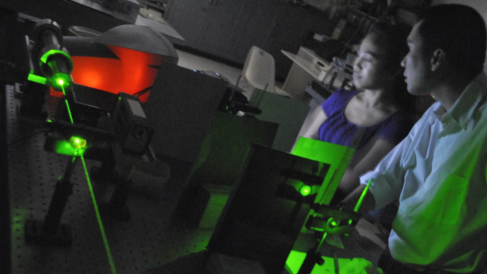 Researcher and student watching a green laser beam on an optical table