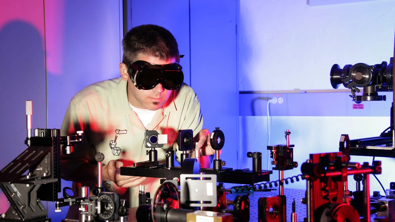 Researcher in laser safety goggles adjusting lens mounts on an optics table