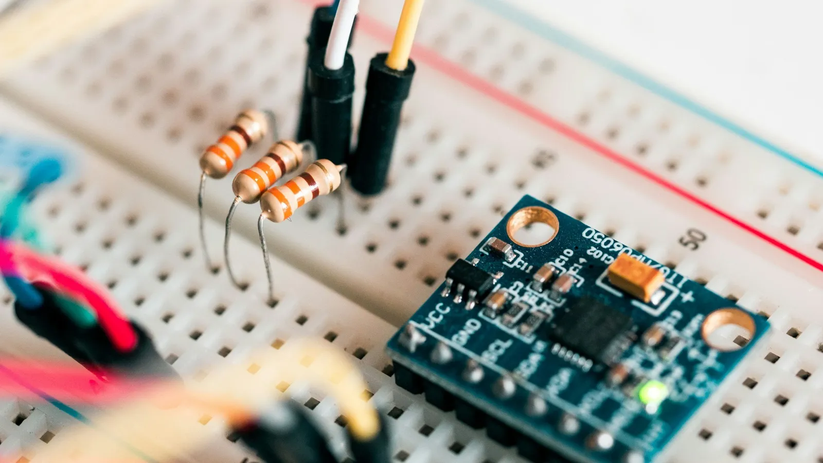 Resistors and jumper wires on a breadboard connected to a small blue circuit board