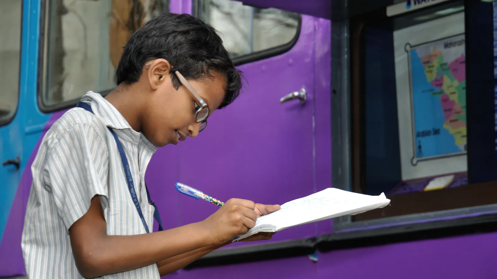 School student in glasses writing notes at a science exhibition in Kolkata