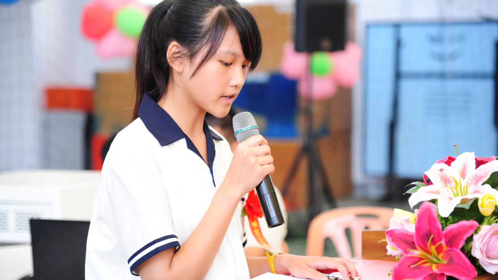 School student in uniform reading a speech into a microphone at a podium