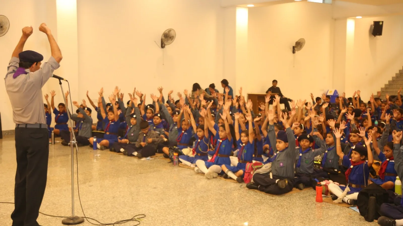 Scouts and guides in uniform raise their arms during a session with their leader