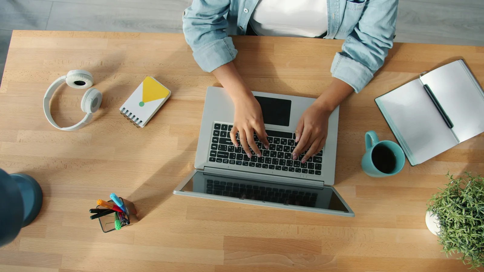 Seen from above, a person types on a laptop at a wooden desk at home