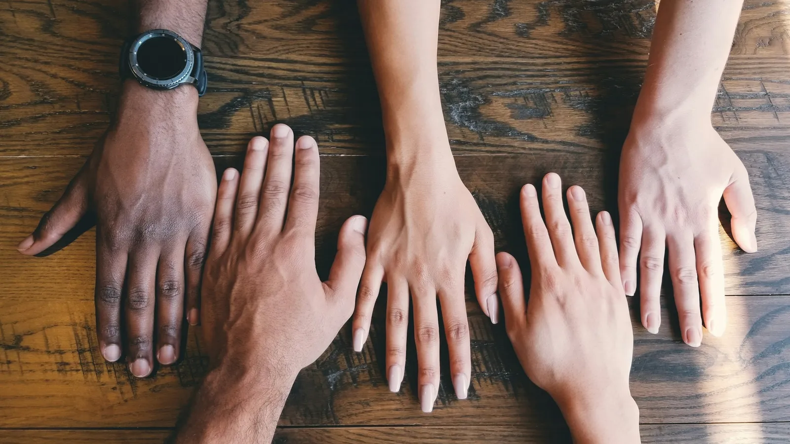 Several hands of different skin tones on a wooden table