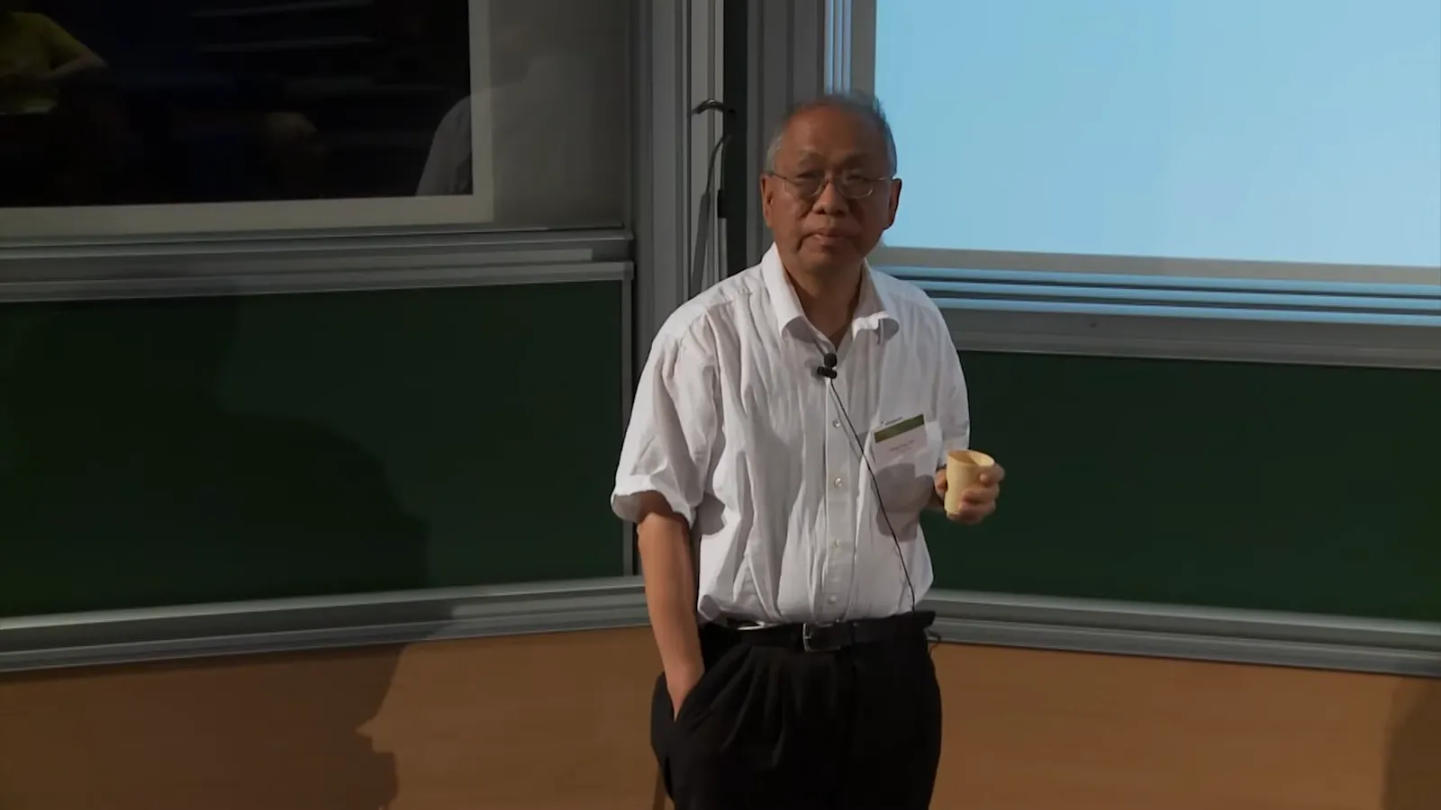 Shing-Tung Yau in a white shirt standing before blackboards during a lecture at IHÉS