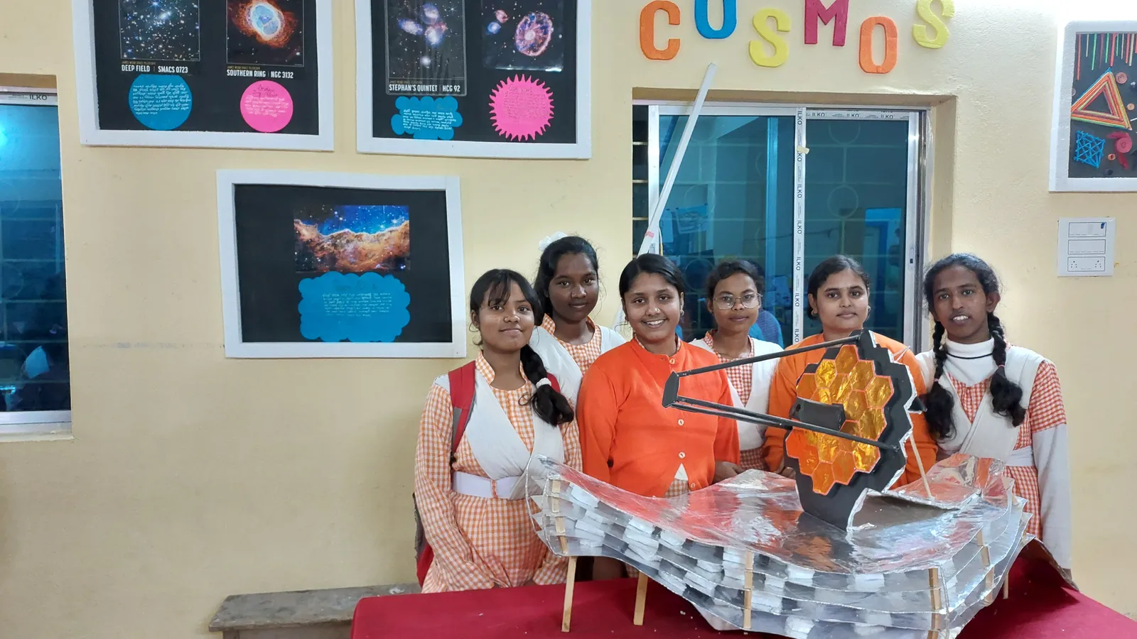Six schoolgirls stand behind their cardboard James Webb Space Telescope model at a school science exhibition