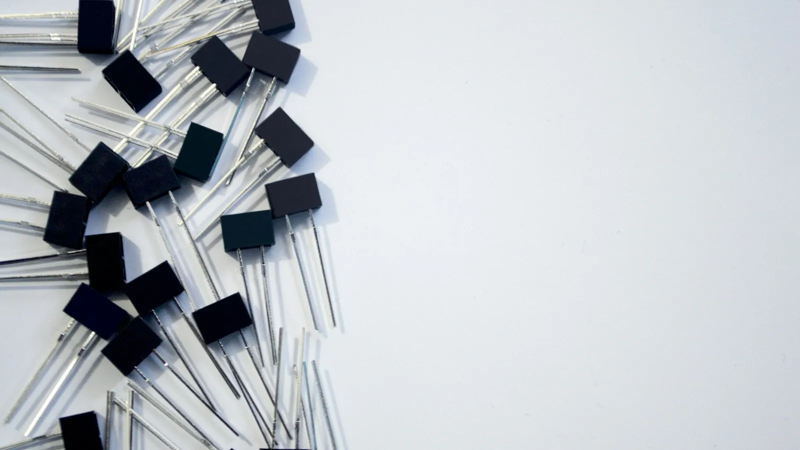 Small black electronic components with wire legs scattered on white