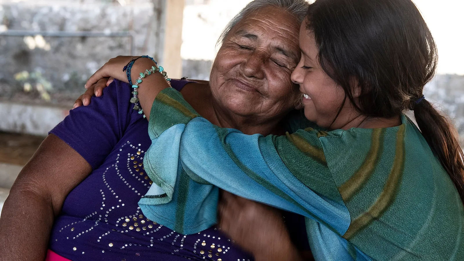 Smiling girl in a striped shawl hugging her grandmother cheek to cheek