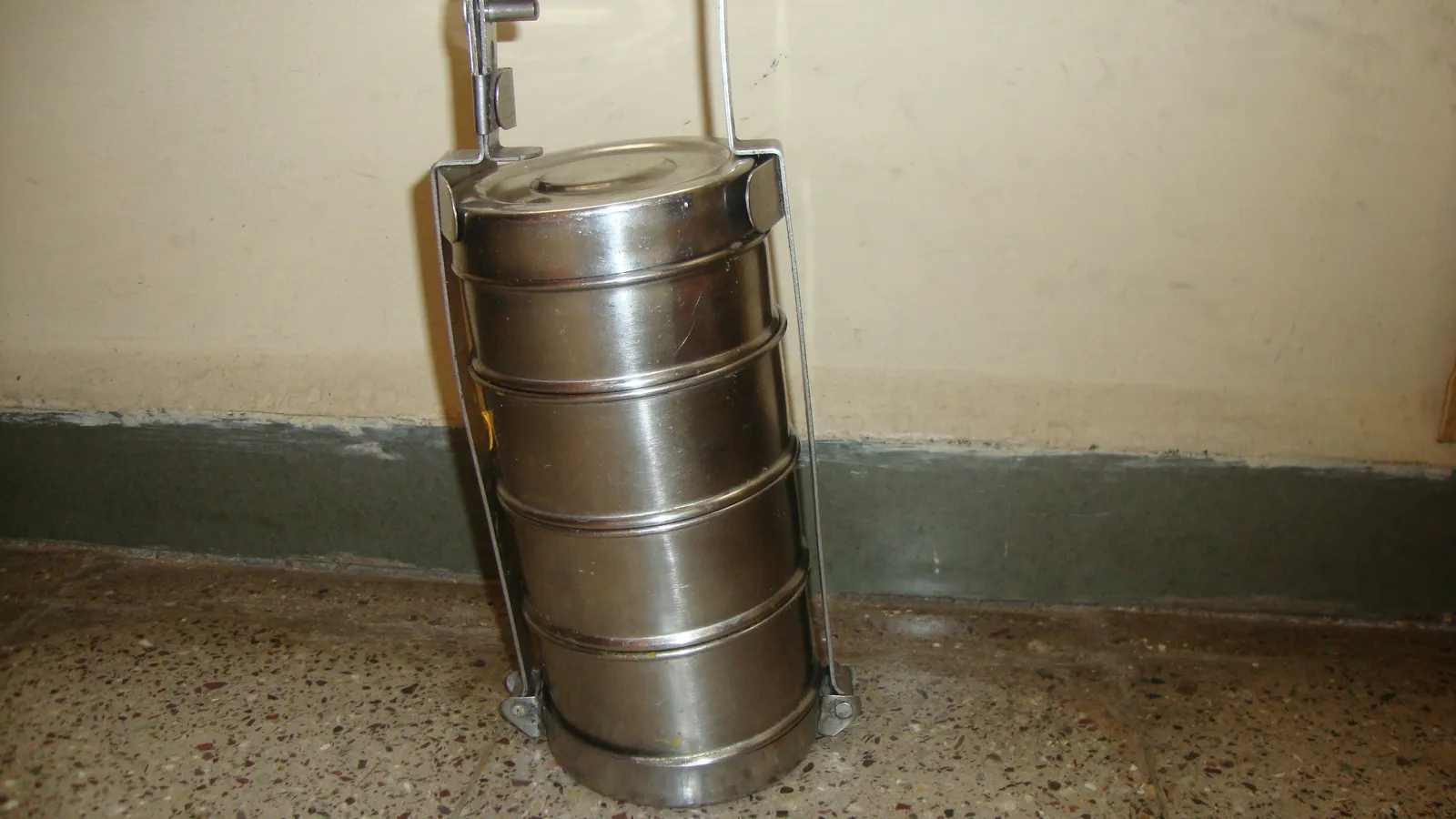 Stacked stainless steel tiffin carrier standing on a terrazzo floor