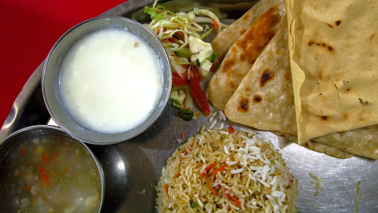 Steel thali with rotis, vegetable rice, curd, salad and vegetable soup