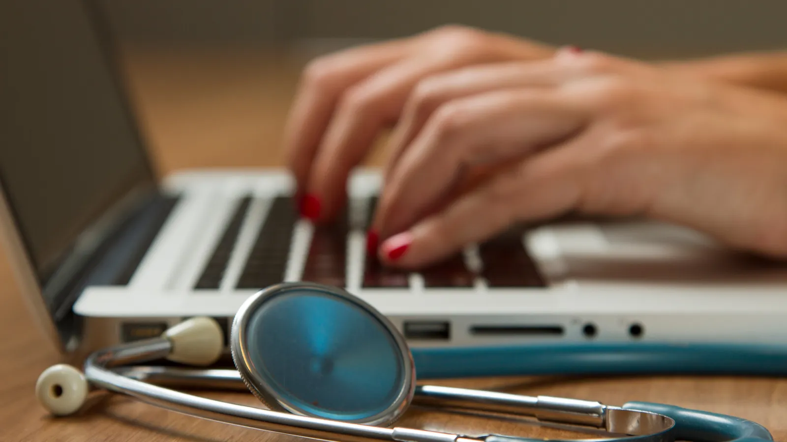 Stethoscope on a desk in front of a laptop while someone types