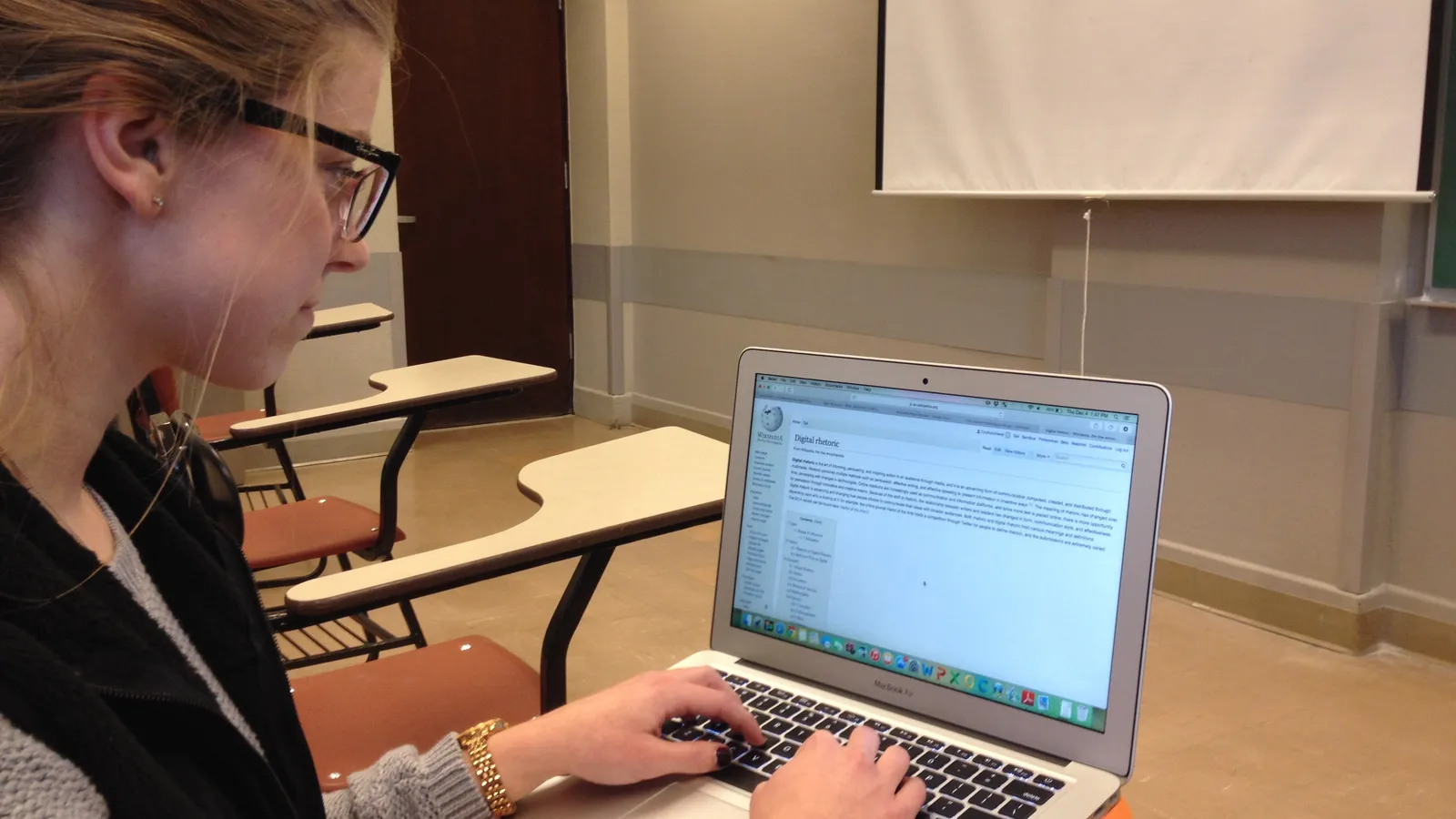 Student in glasses typing on a laptop at a classroom desk