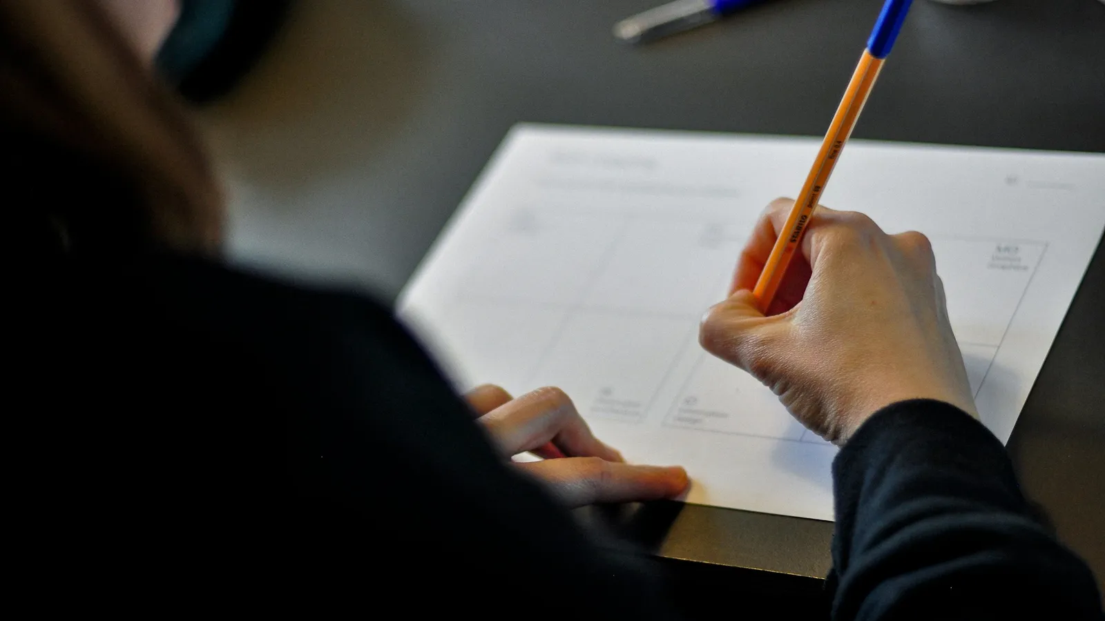 Student writing answers on a test paper with a pencil