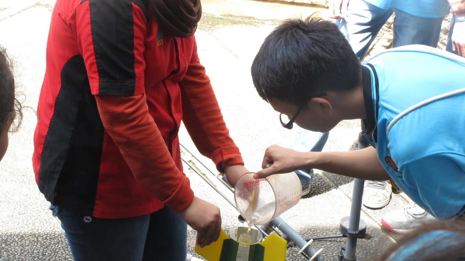 Student pouring water from a measuring jug into a bottle rocket on its launcher