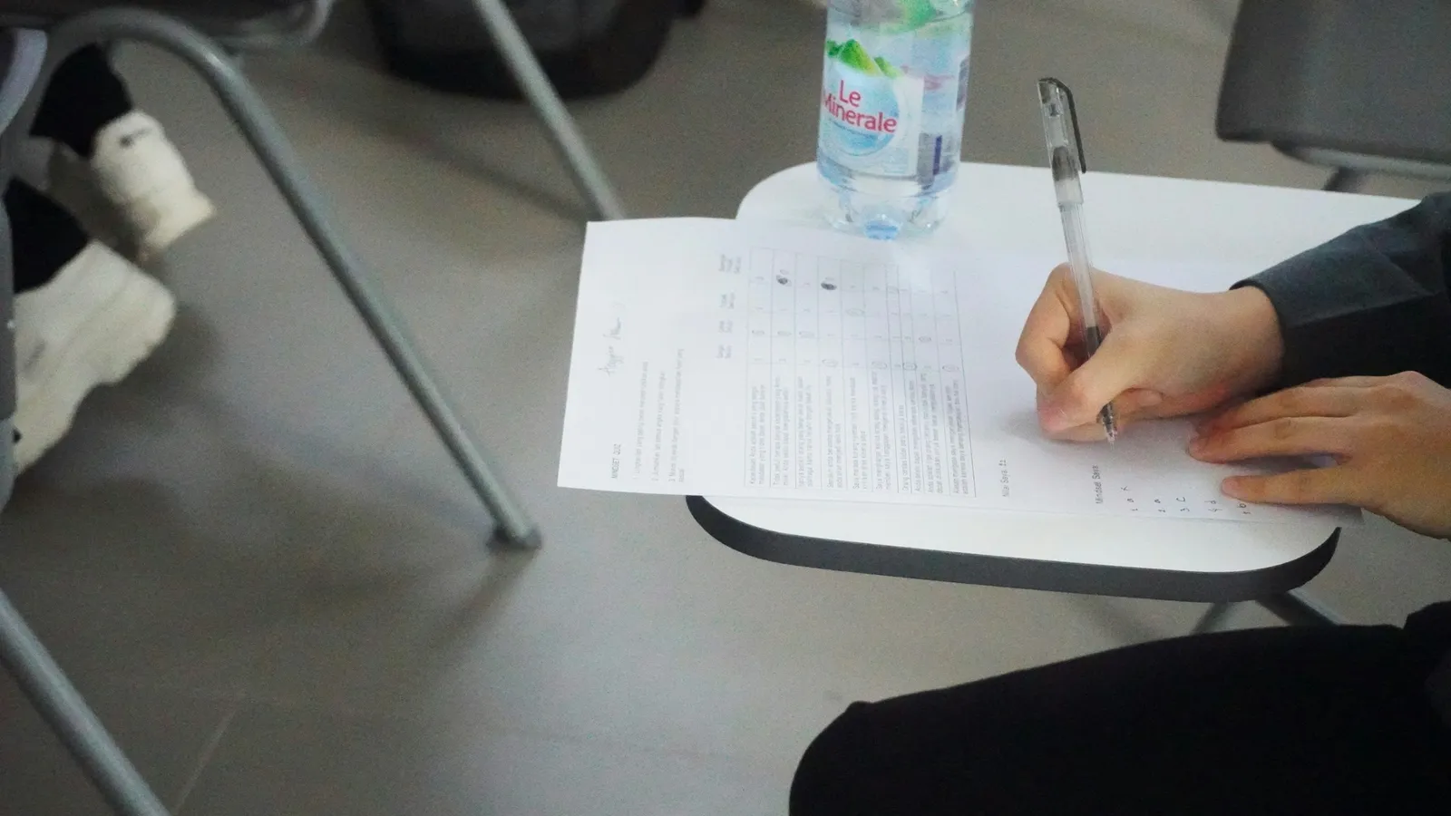 Student writing answers on a test paper at an exam desk