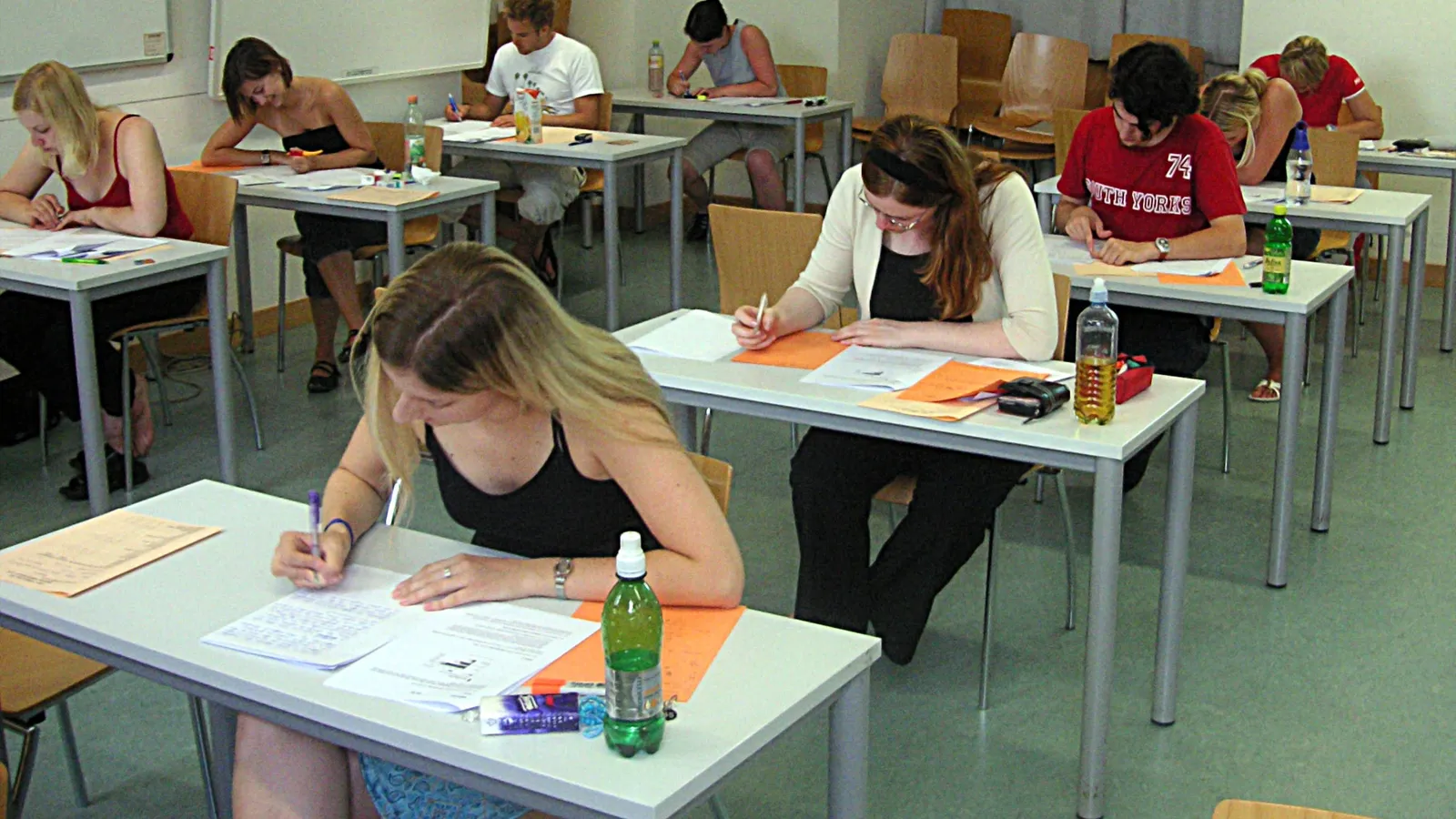 Students at separate desks writing answers on exam papers in a classroom