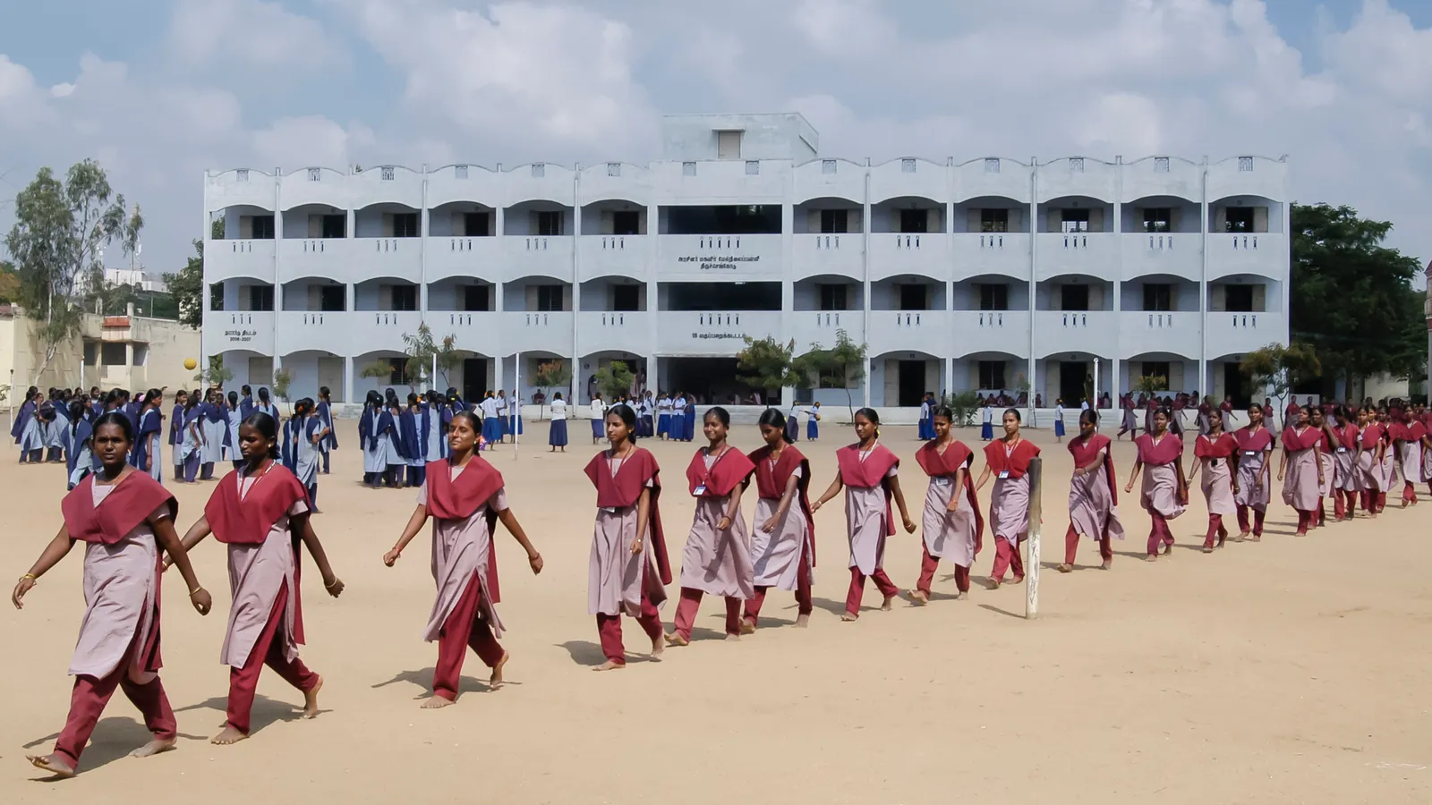 Students in matching uniforms walk in a line across a school ground in Salem, Tamil Nadu
