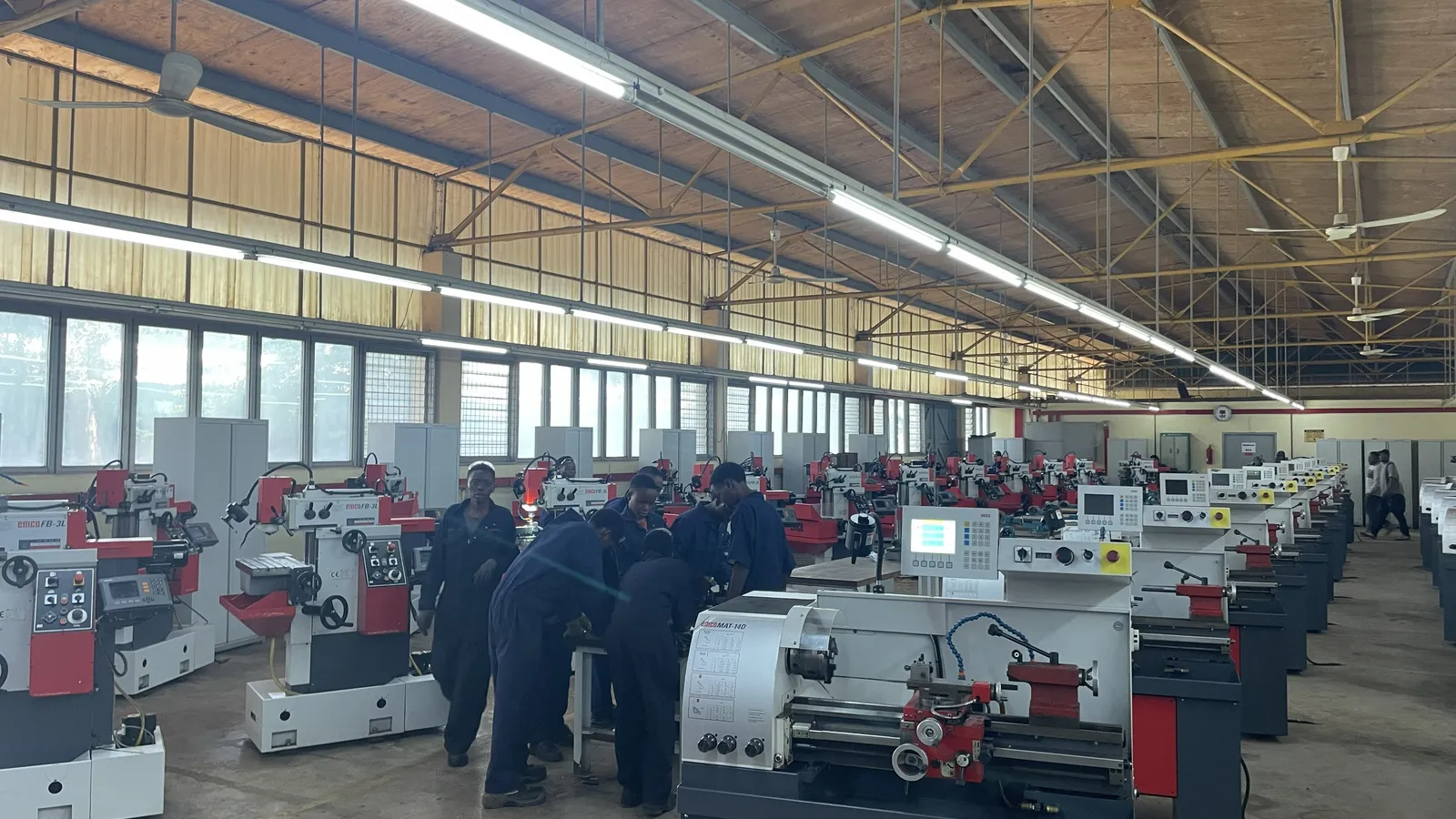 Students in navy overalls at a workbench among lathes and milling machines in a workshop