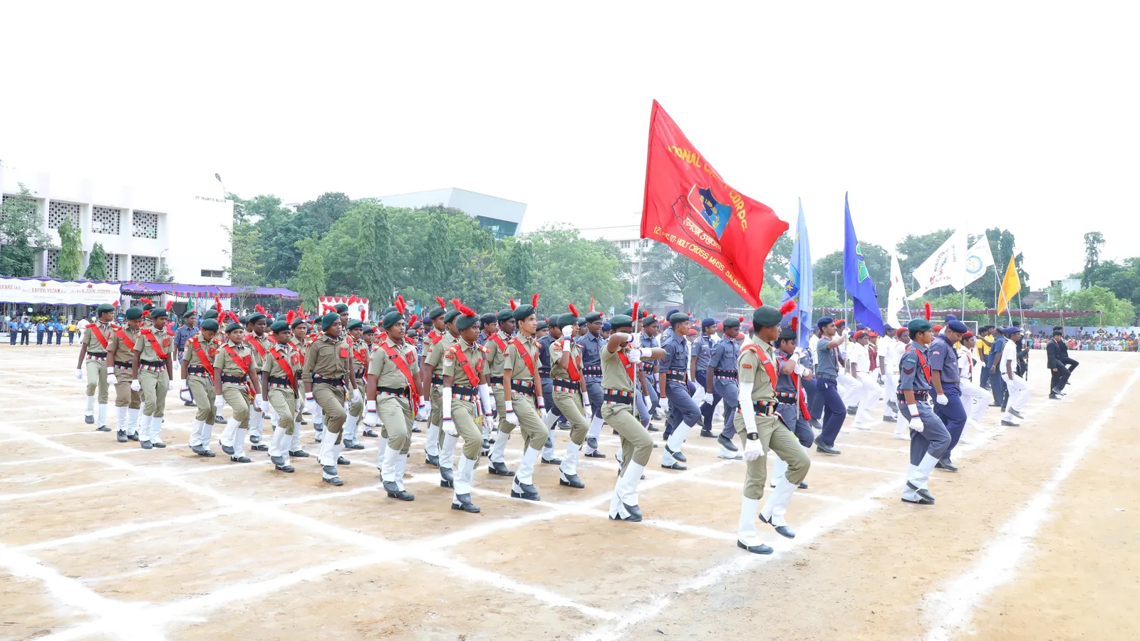 Students in uniform march past with flags on a school sports day ground