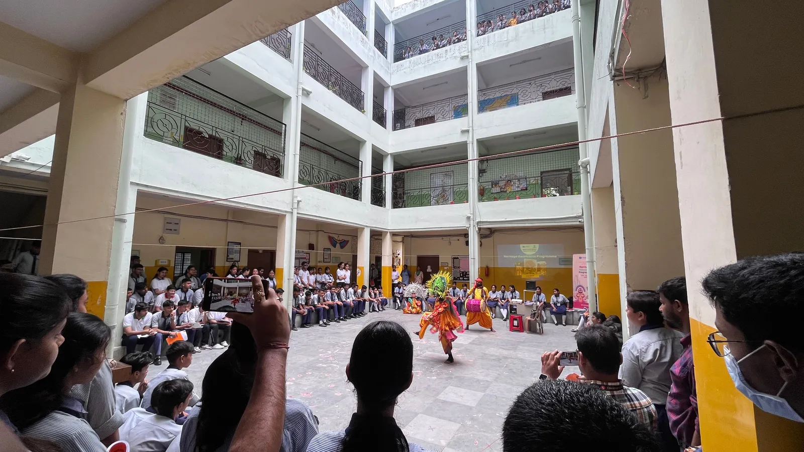 Students in uniform watch a Chau dance performance in a school courtyard