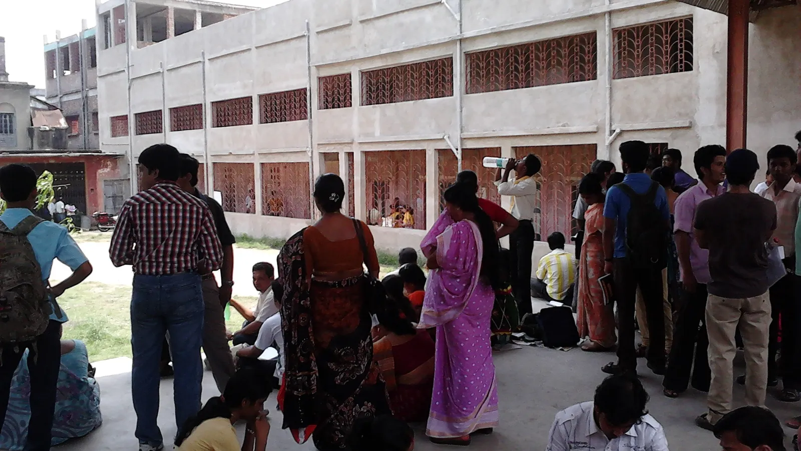 Students revising notes outside an entrance exam centre as families wait