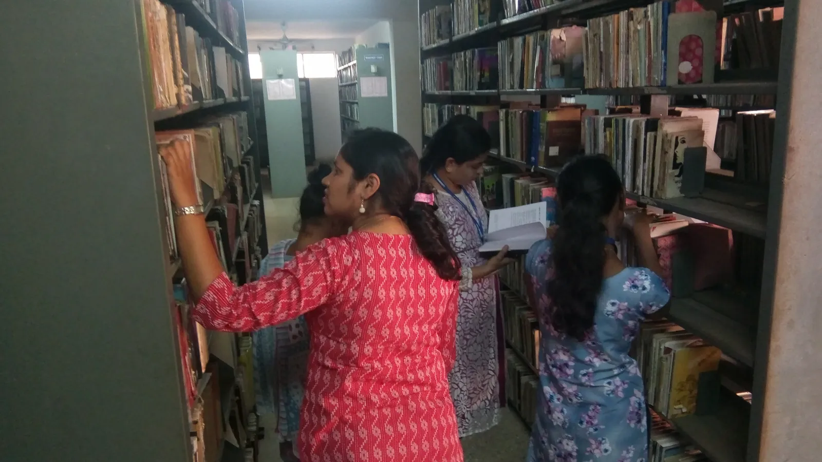 Students searching tall shelves of reference books in a library aisle