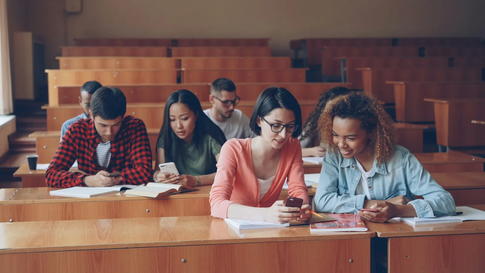Students taking notes at desks in a tiered university lecture hall