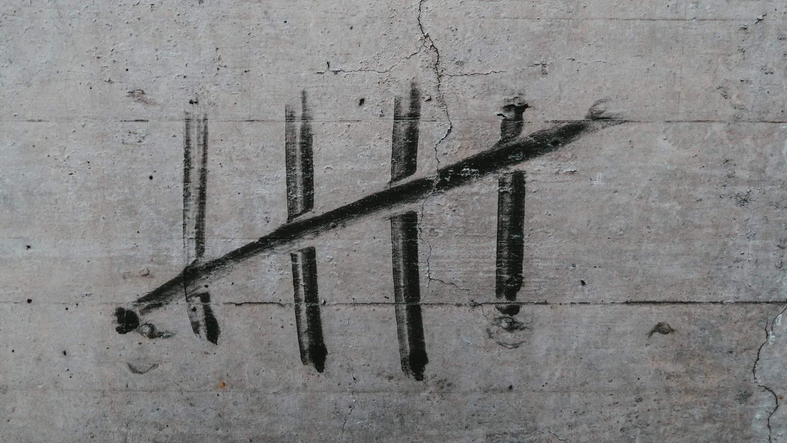 Tally marks drawn in chalk on a grey wall