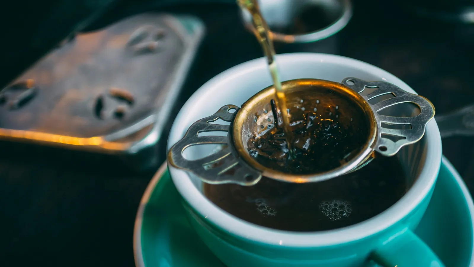 Tea being poured through a strainer into a cup