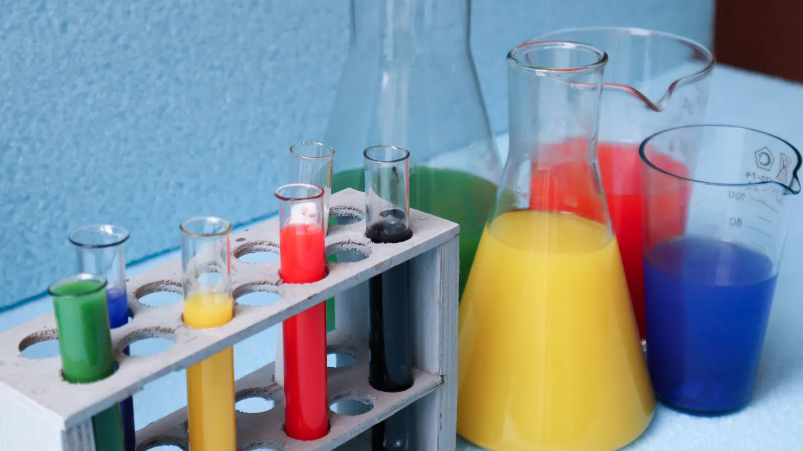 Test tubes in a rack beside conical flasks and beakers of coloured liquid