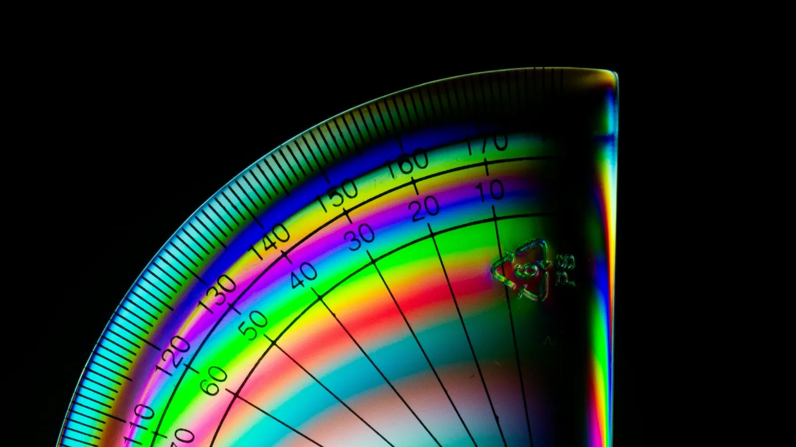 The curved edge of a clear protractor glowing in rainbow colours