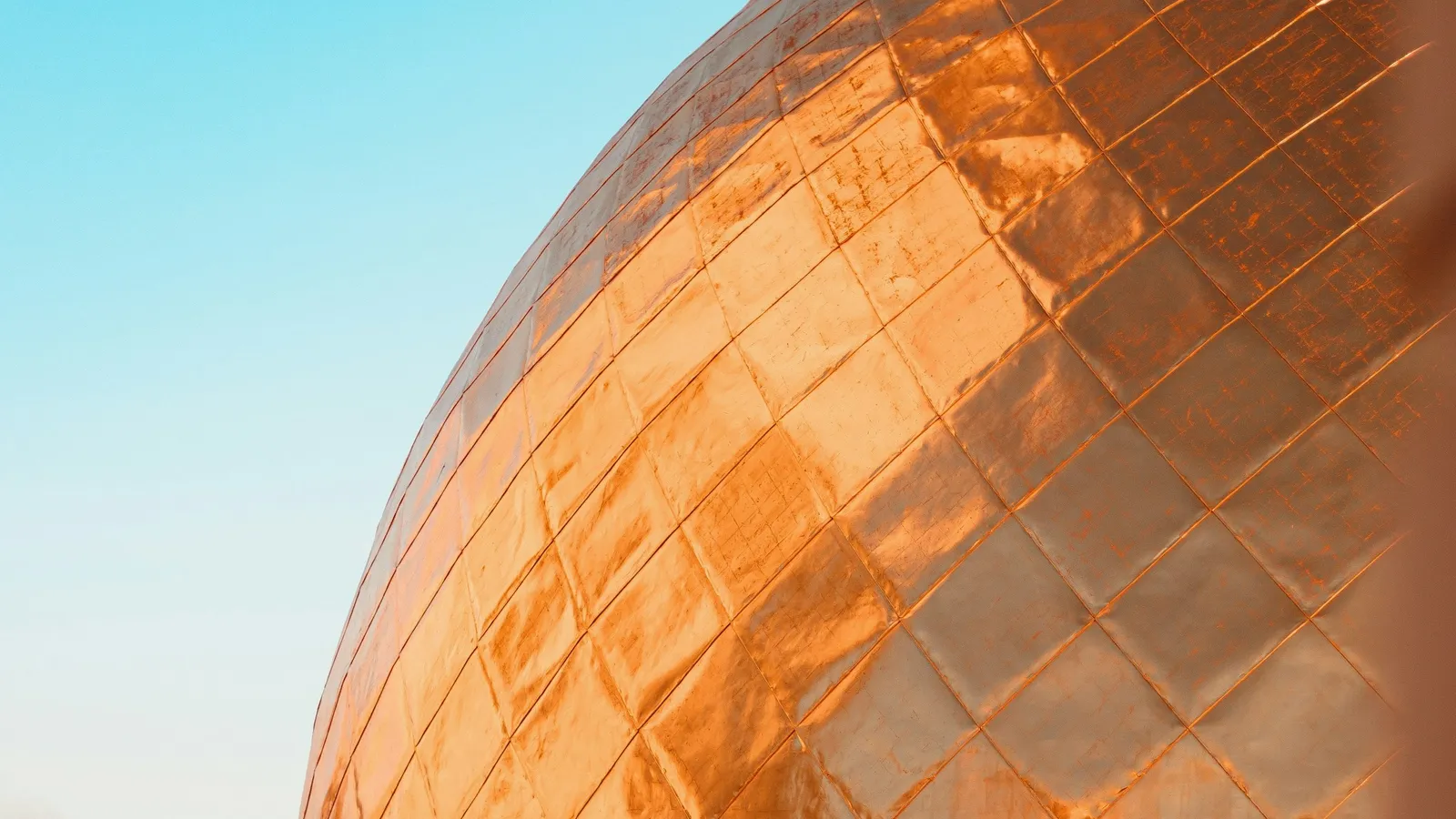 The curved surface of a large copper dome against the sky