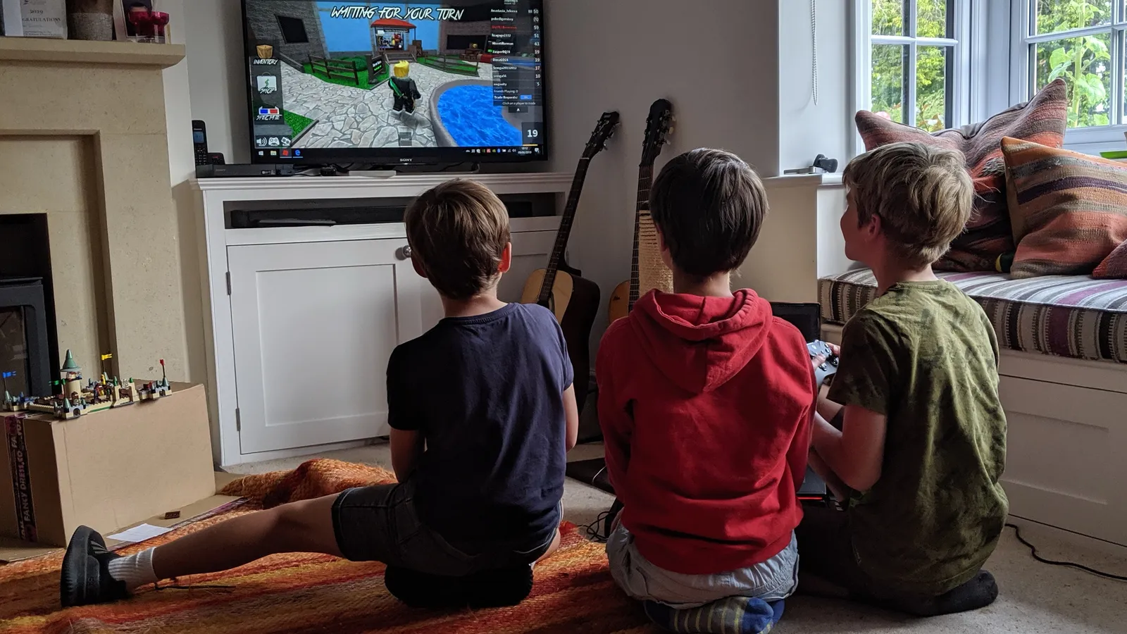 Three children seen from behind playing an online multiplayer game on a living-room TV