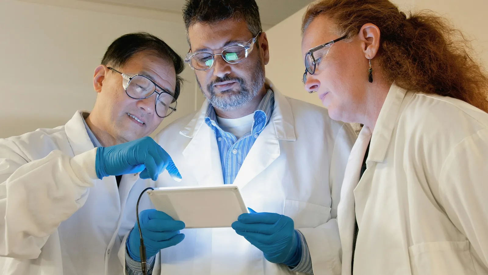 Three researchers in lab coats looking at a tablet together in a laboratory