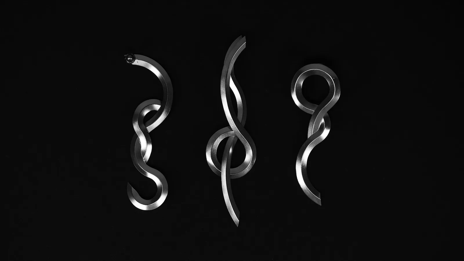 Three twisted metal shapes lit against black