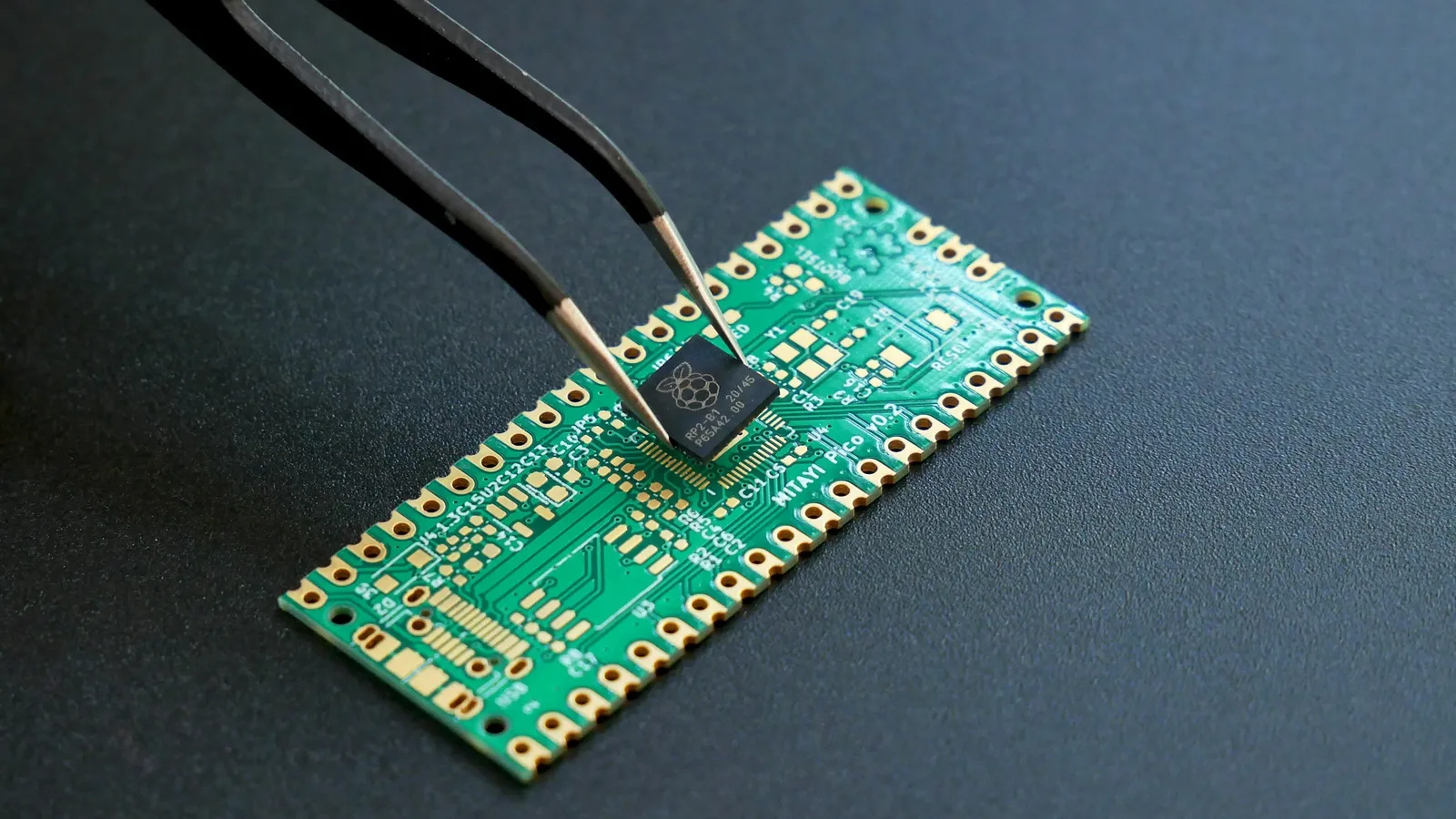 Tweezers holding a small green circuit chip