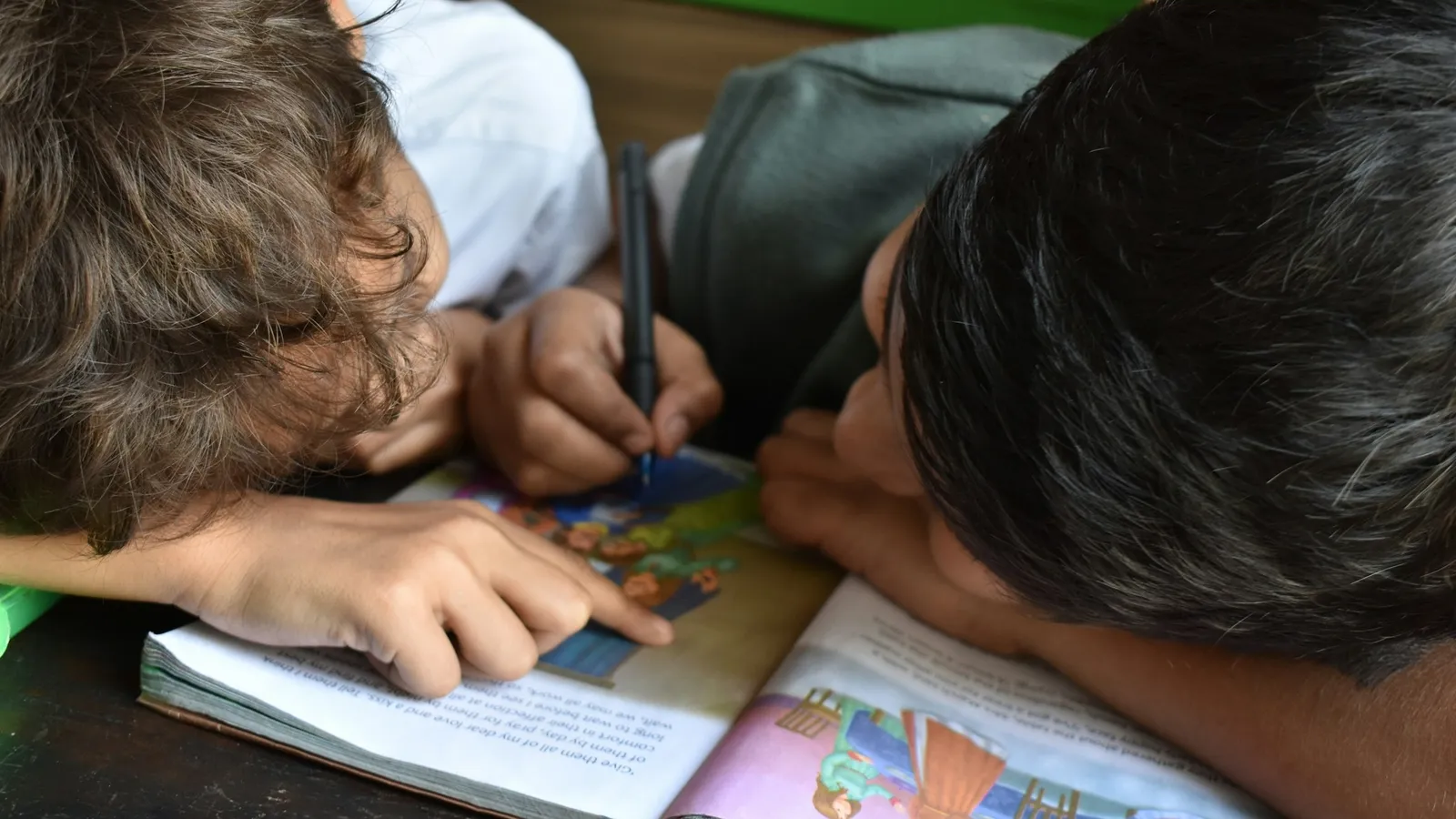 Two children leaning over their books at the same table