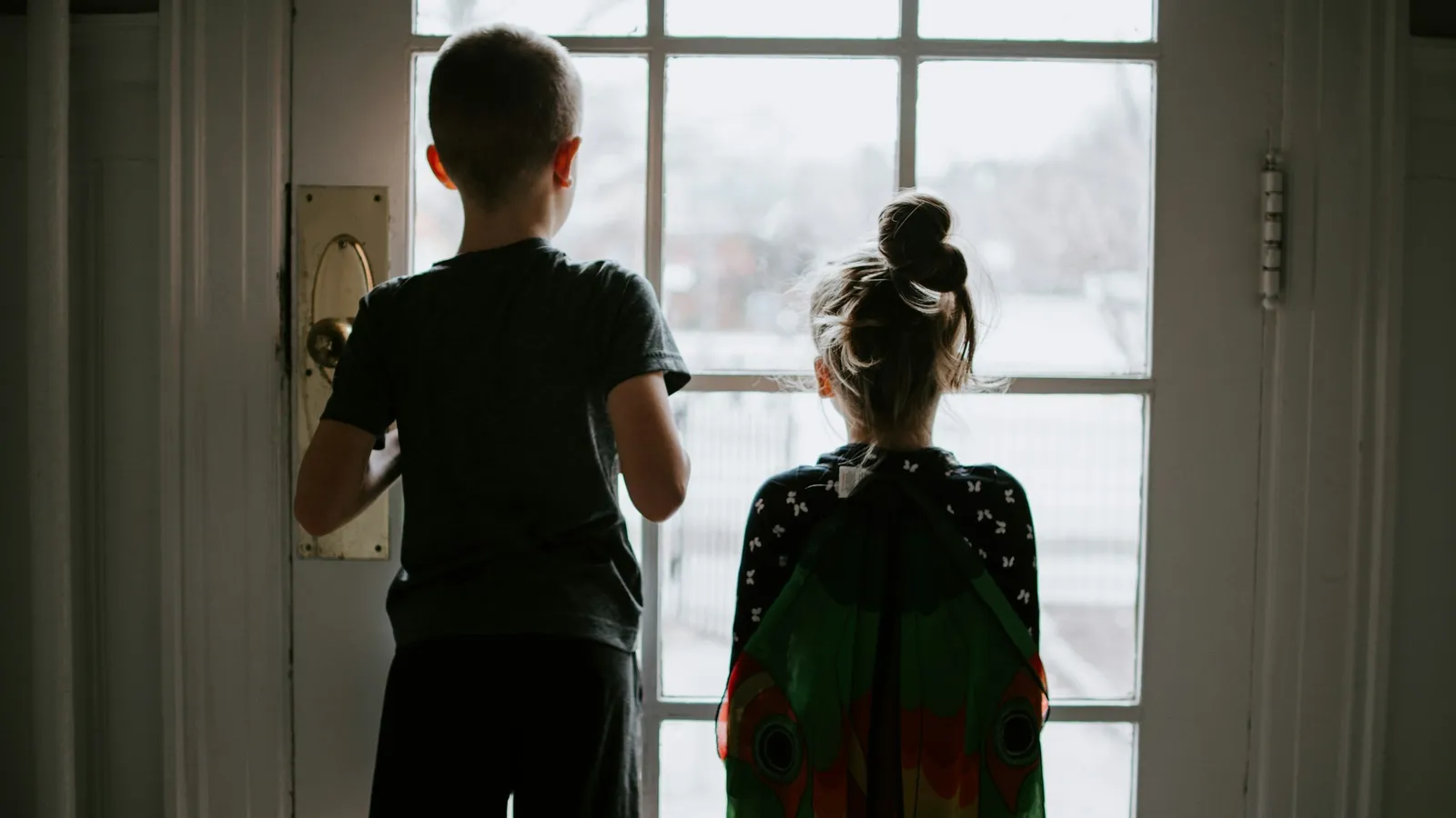 Two children looking out of a window at home