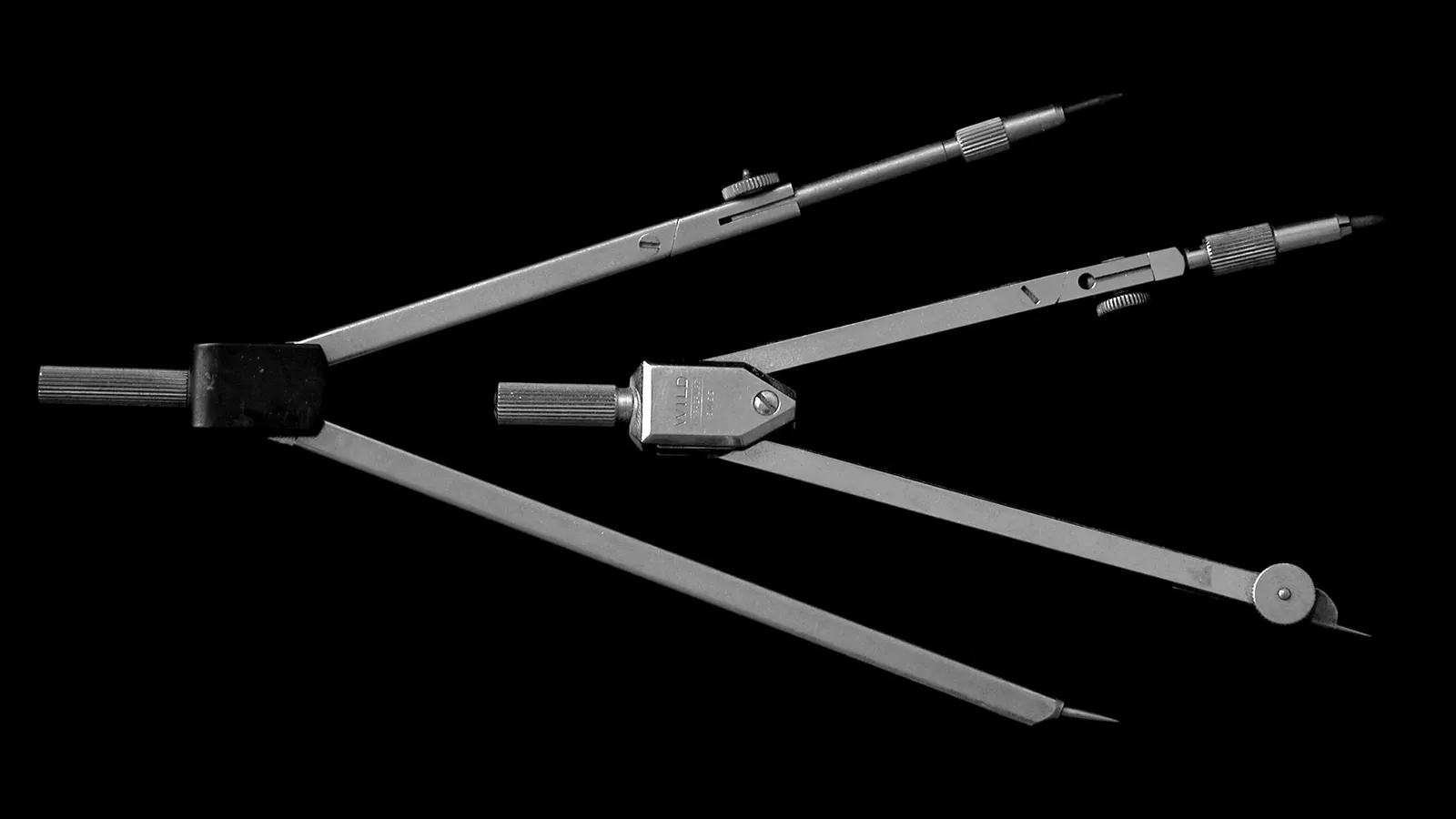 Two drawing compasses lying on a black background