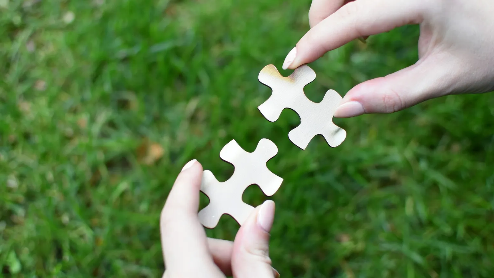 Two hands fitting jigsaw pieces together over grass