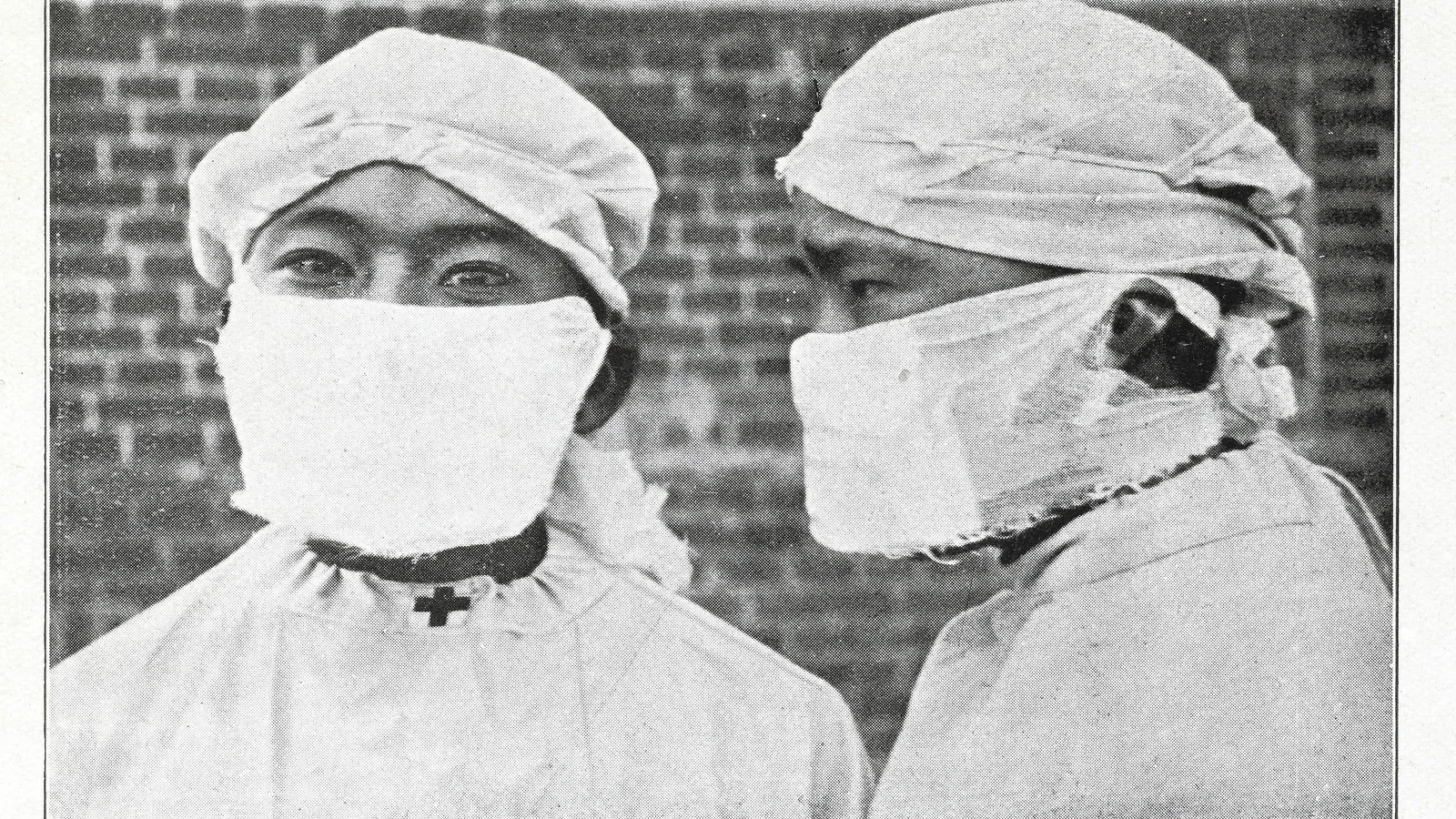 Two health workers in caps and gowns wearing gauze-cotton masks tied over nose and mouth