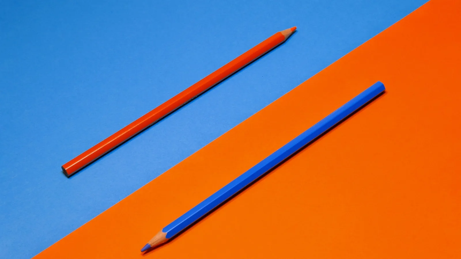 Two pencils lying across an orange and blue background