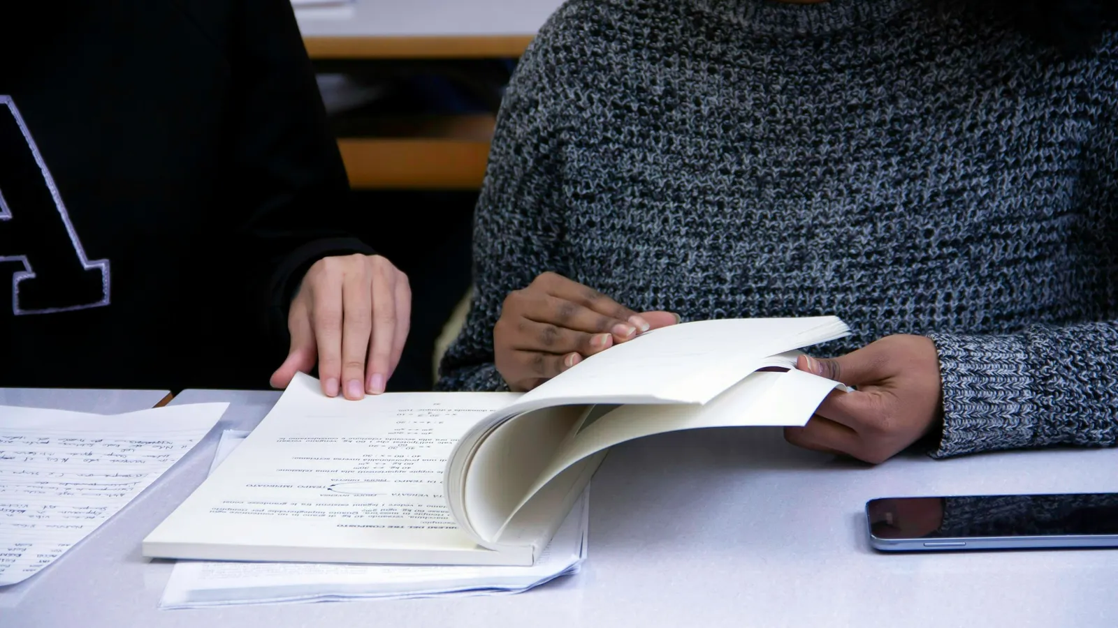 Two people looking over an open notebook together at a table