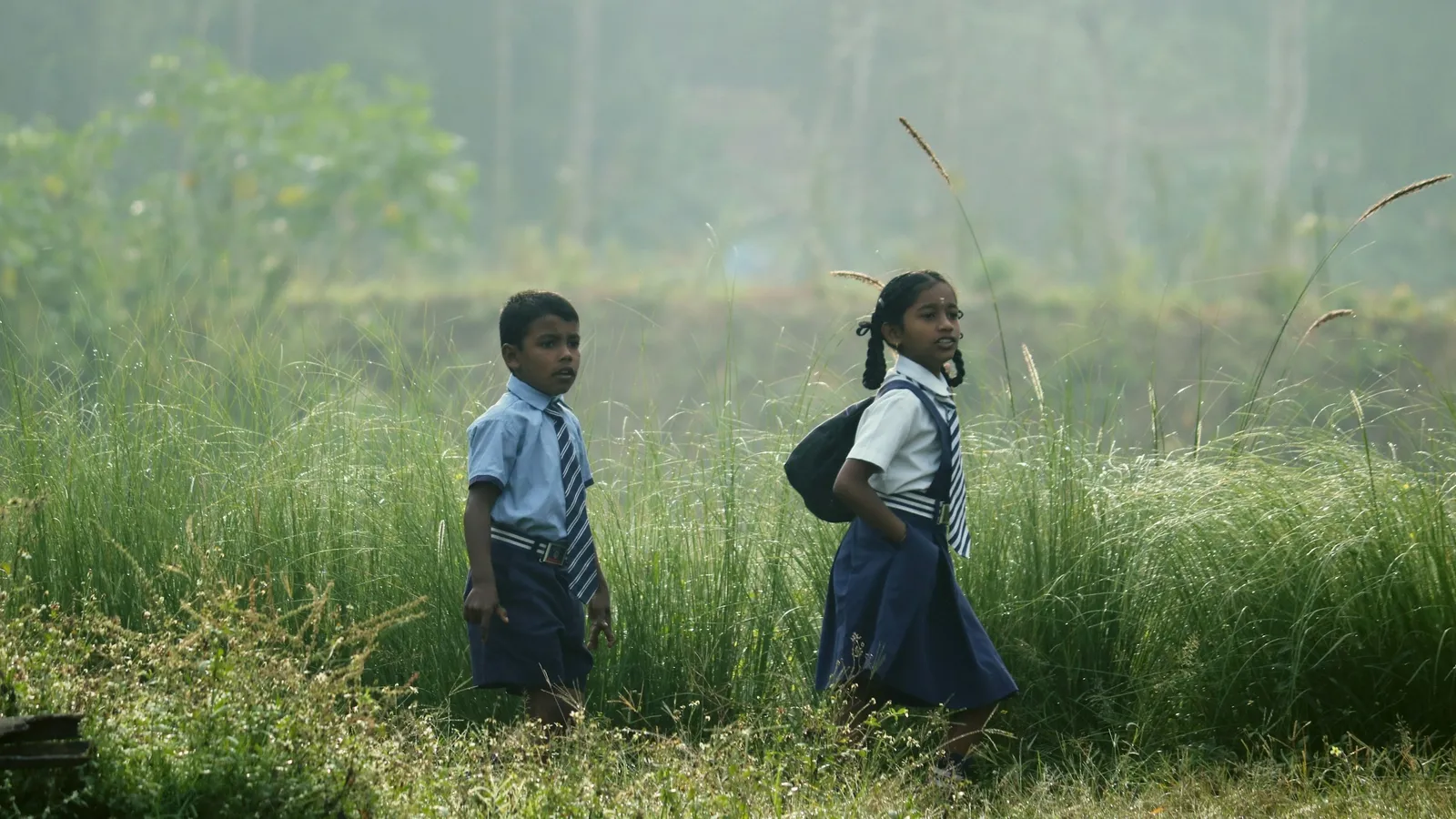 Two schoolchildren in uniform walking along a grassy path