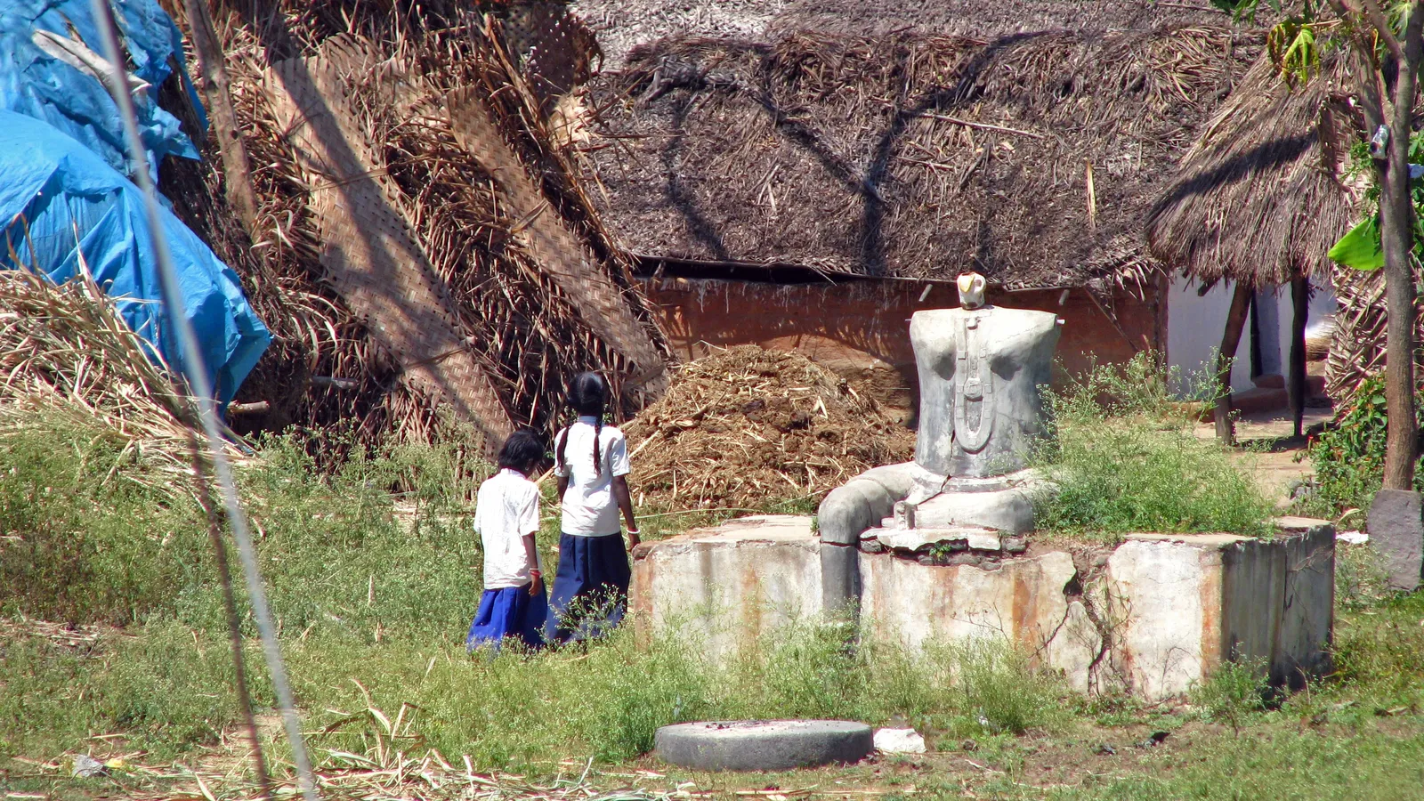 Two schoolgirls in uniform walking home past thatched houses in Vellore