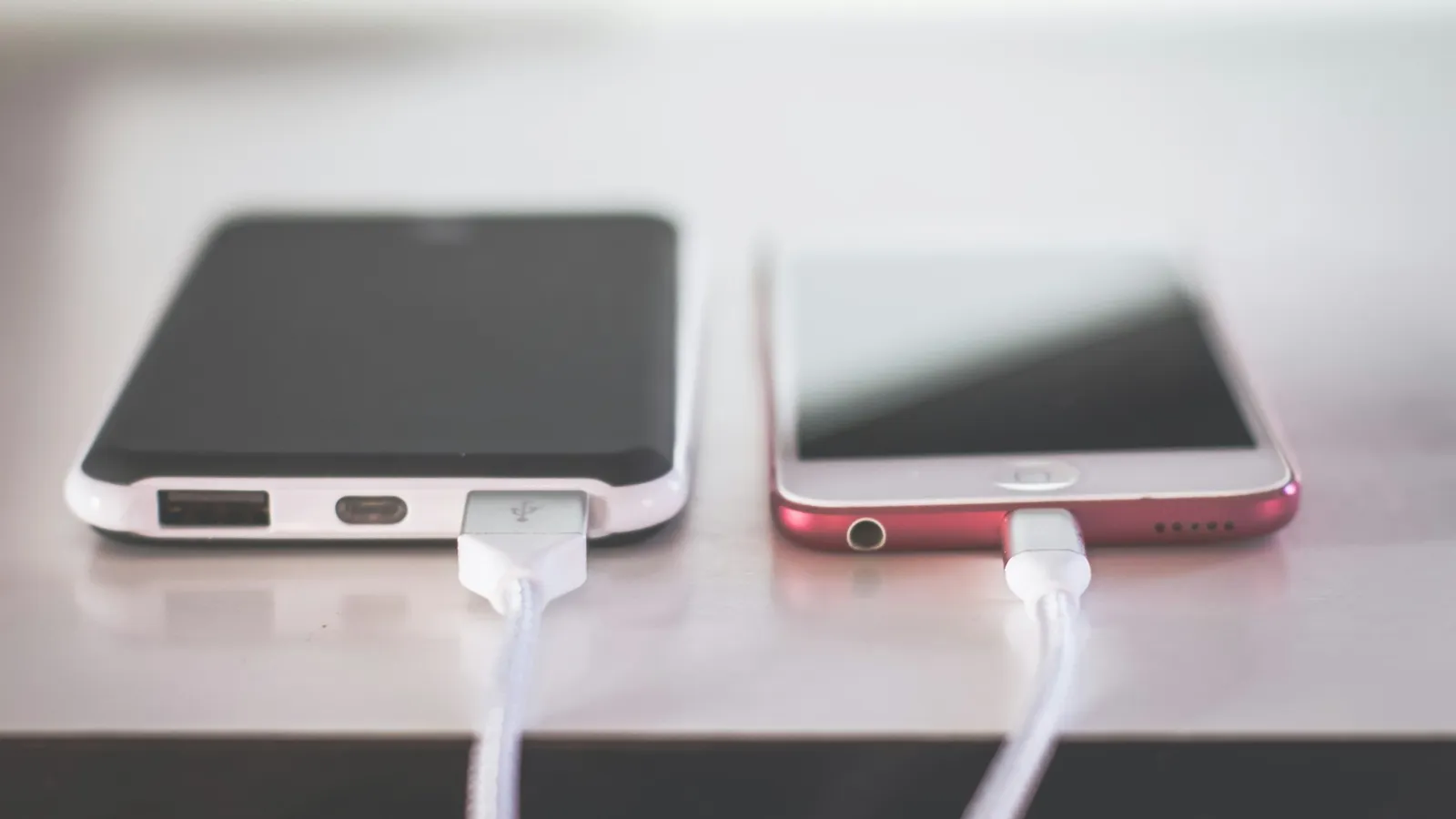 Two smartphones charging on a white table