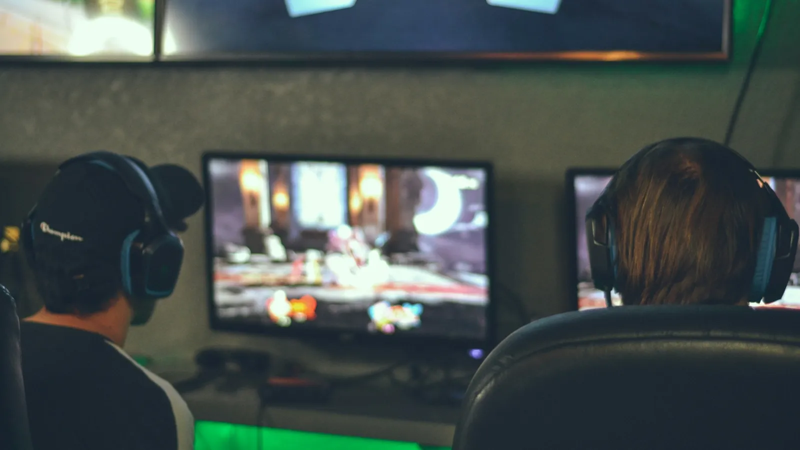 Two young people wearing headsets playing video games on large screens