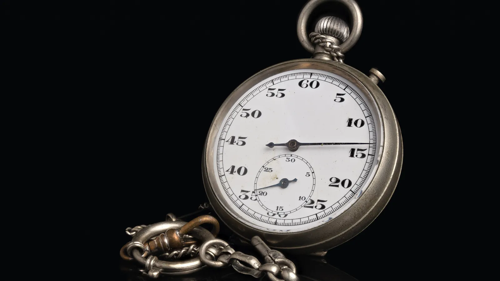 Vintage silver stopwatch with a white dial and chain on a black background